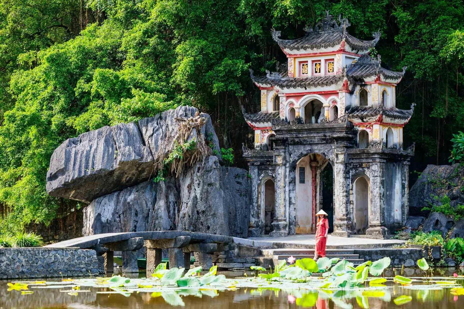 Temple ancien adossé à une falaise, se reflétant dans un étang de lotus