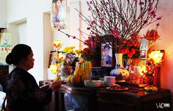 Une femme se recueille devant un autel domestique fleuri, lors des fêtes du Têt