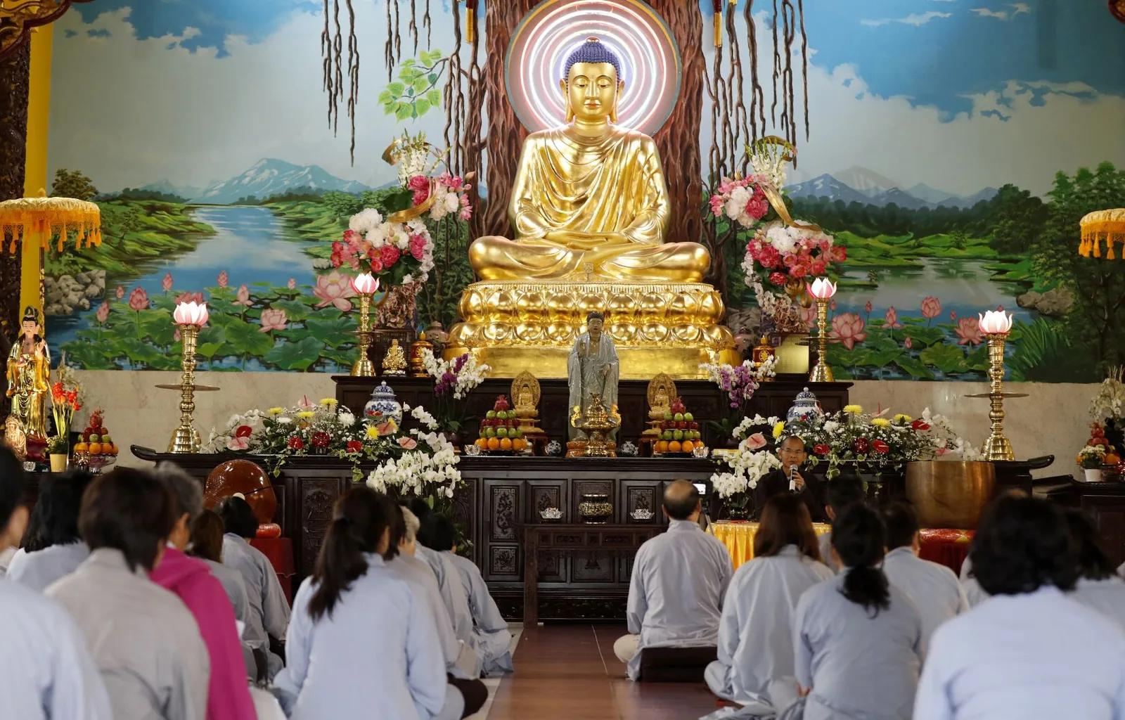 Fidèles assis en méditation devant une grande statue dorée de Bouddha