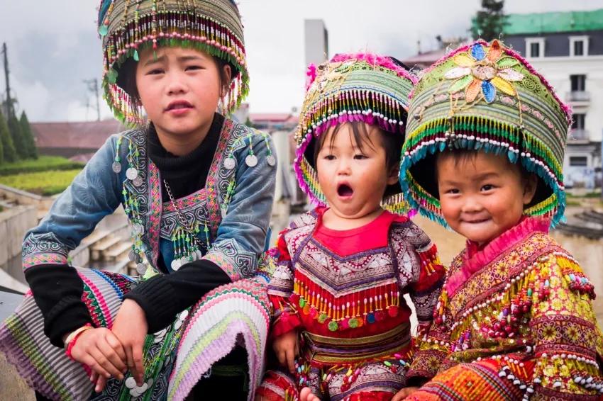 Trois enfants d’une minorité ethnique en costumes brodés colorés, assis côte à côte