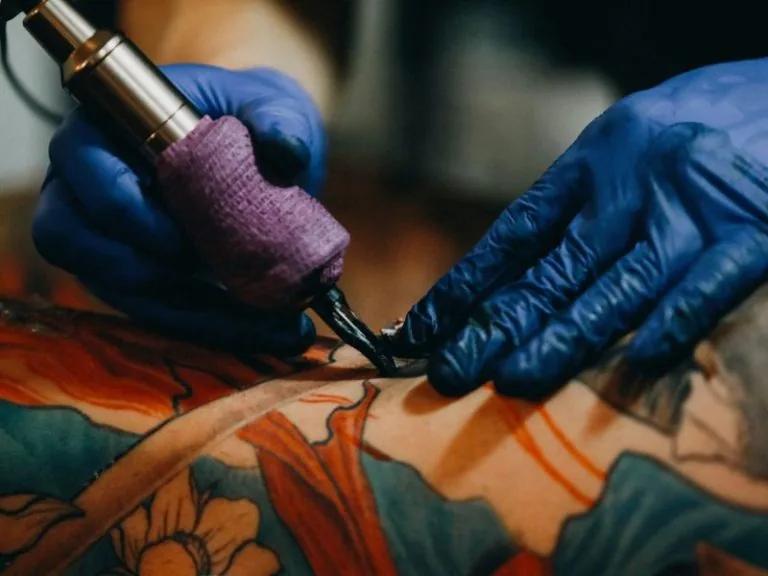 Gros plan sur une main gantée tatouant un motif traditionnel sur une peau