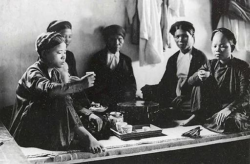 Photographie d’archive : femmes vietnamiennes réunies autour d’une table basse, coiffées du turban traditionnel