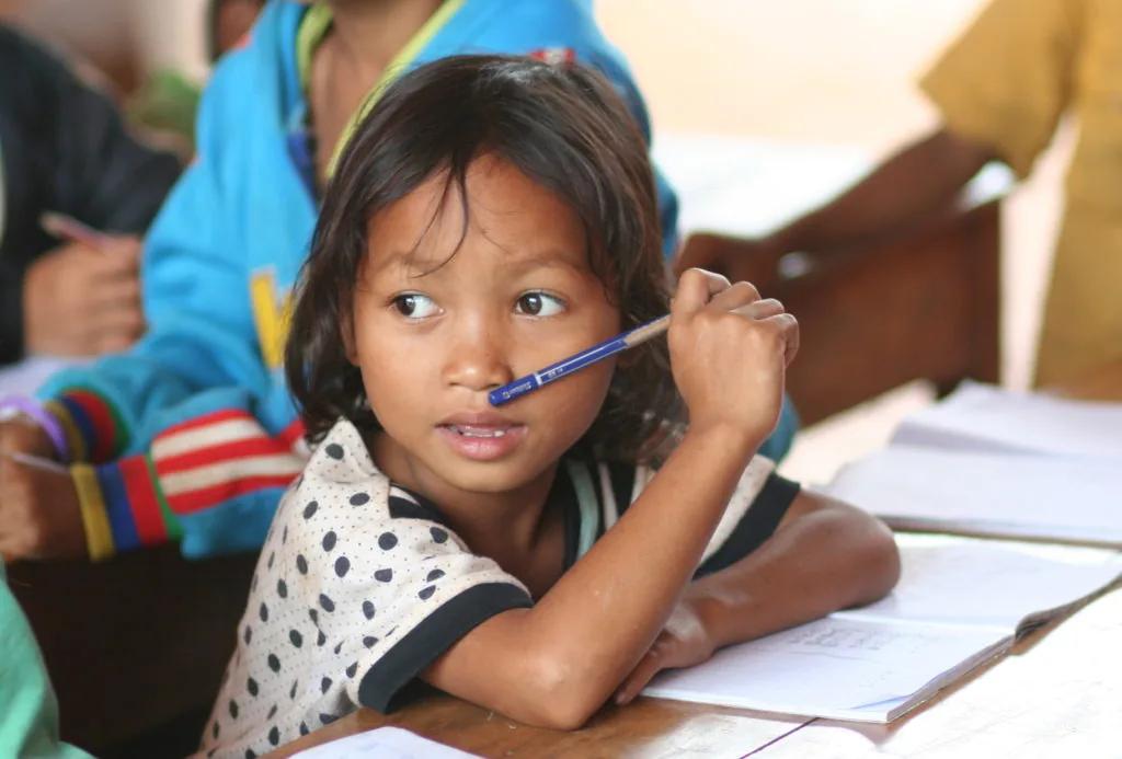 Une écolière lève les yeux de son cahier, stylo à la bouche, en classe