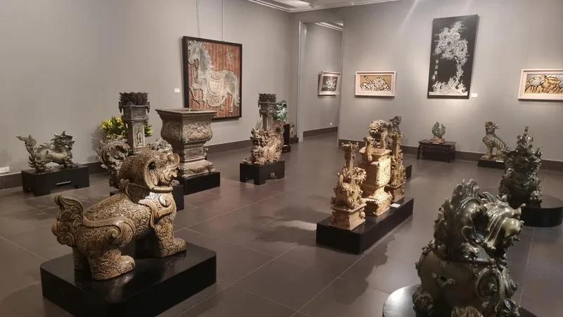 Salle de musée présentant des sculptures de pierre sur socles et des photographies encadrées