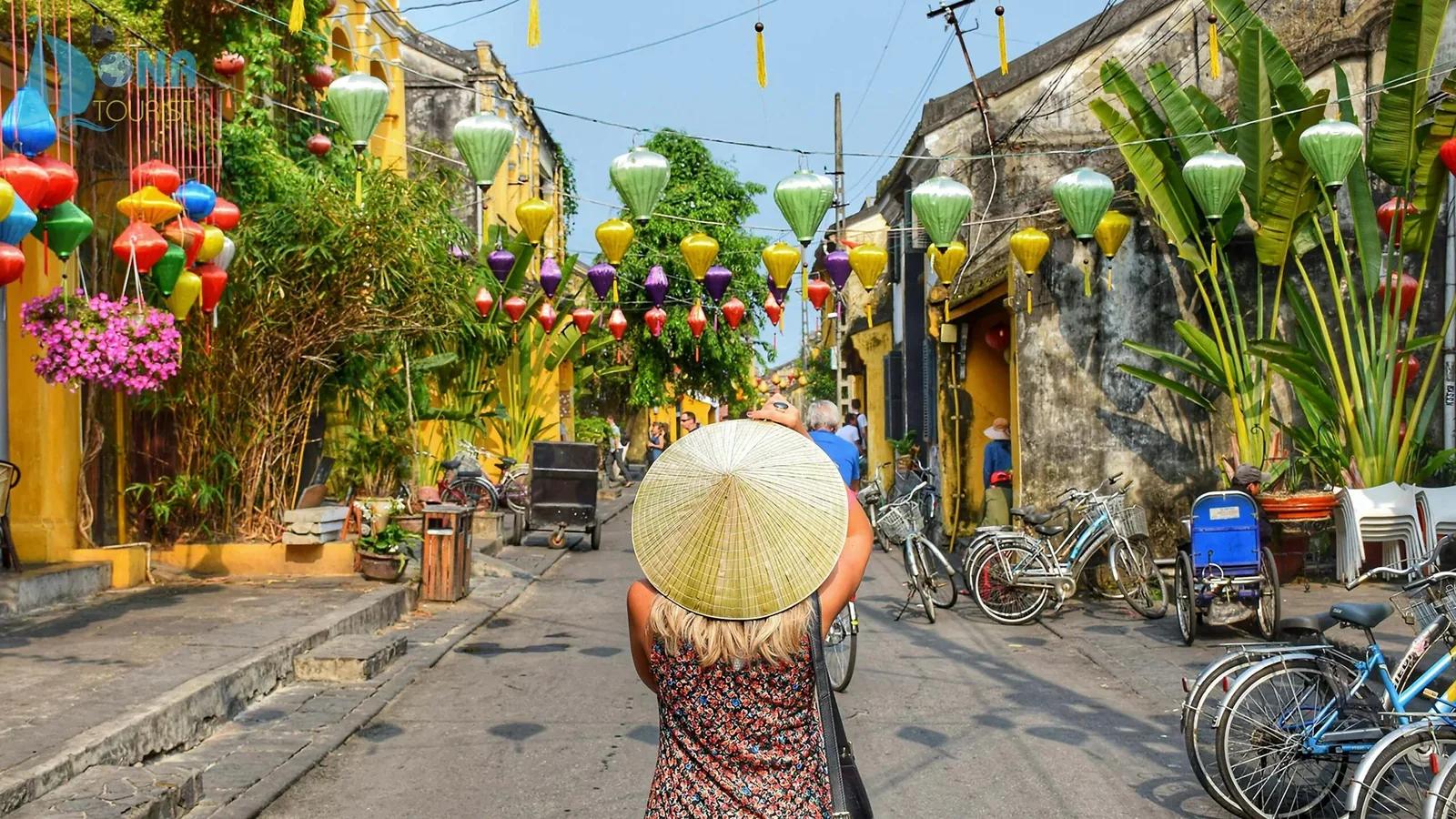 Ruelle d’une vieille ville ornée de lanternes, femme au chapeau conique portant une palanche
